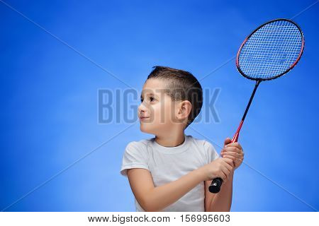 Boy with badminton racket standing against blue studio background