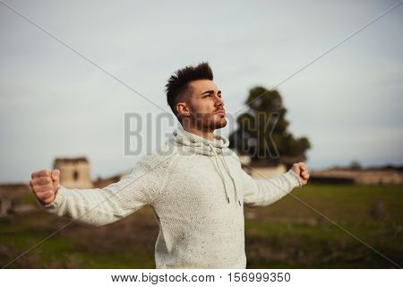 Strong guy open his arms in the meadow. 