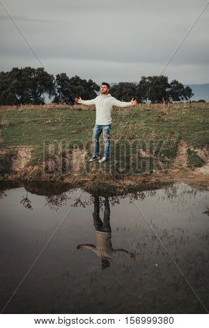 Attractive guy with jeans and white jersey next to a river in the meadow