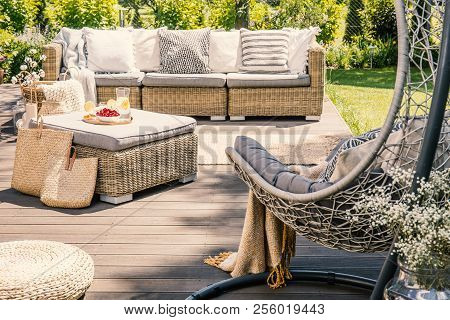 Pillows On Rattan Couch Near Table On Patio With Hanging Chair In The Garden. Real Photo