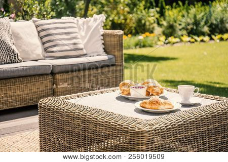 Beige Color Wicker Table And Settee On A Porch During Sunny Afternoon In The Garden. Croissants And