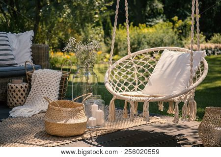 A Beige String Swing With A Pillow On A Patio. Wicker Baskets, A Rug And A Blanket On A Wooden Deck