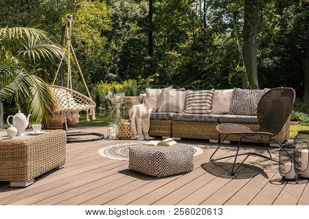 A Rattan Patio Set Including A Sofa, A Table And A Chair On A Wooden Deck In The Sunny Garden.