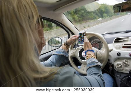 Bottrop, Germany - Aug 16, 2018: A Blond Woman Is Checking Her Smartphone While She Is Driving On A 