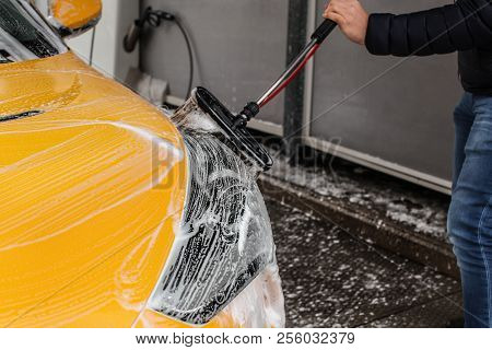 Man Cleaning His Car In Self Serve Carwash, Brush Leaving Shampoo Strokes On Front Headlight.
