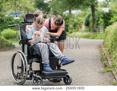 A Young Girl Helping Her Disabled Sister In A Wheelchair