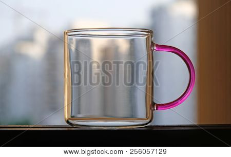 A Glass Mug With A Colored Handle, Standing In The Window Aperture.