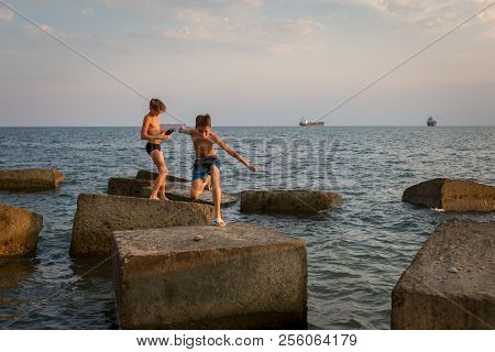 Gizelle-dere Village, Russia, August 07, 2018: Two Boys Play On The Beach, Jumping On Concrete Block