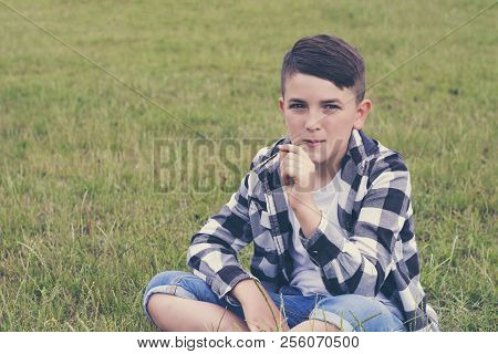 Full-length Portrait Of Attractive Teenage Boy Thinking About Something And Chewing Blade Of Grass. 