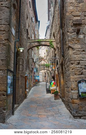 Volterra Italy - April 21 2011; Narrow Laneway Lined By High Stone Buildings With Small Business And
