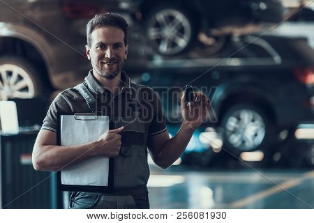 Auto Mechanic Holding Clipboard And Car Keys. Repair Service. Handsome Serious Caucasian Man In Grey