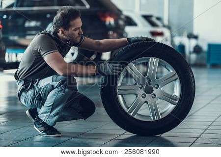 Caucasian Handsome Auto Mechanic Cheking Car Wheel. Portrait Of Adult Machinist Doing Wearing Unifor