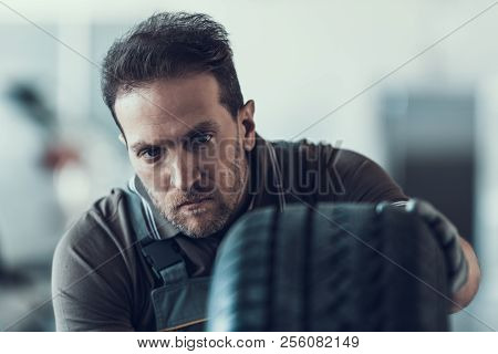 Handsome Auto Mechanic Cheking Car Wheel. Portrait Of Caucasian Adult Machinist Doing Wearing Unifor
