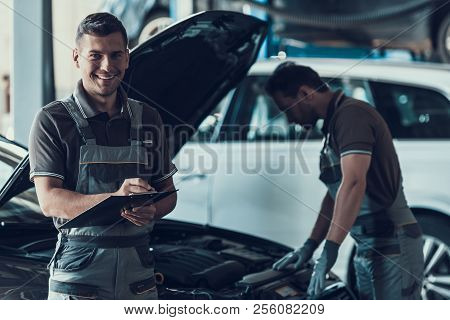 Two Handsome Happy Auto Mecanics In Garage. Portrait Of Attractive Repairmen In Uniform Showing Posi