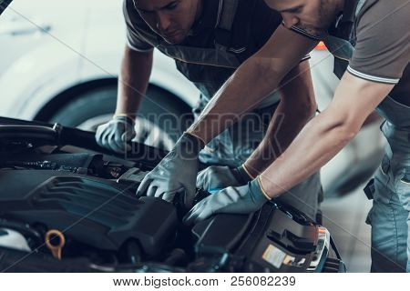 Close-up Of Two Mecanics While Fixing Car. Strong Muscular Workers In Uniform And Gloves Repairing A