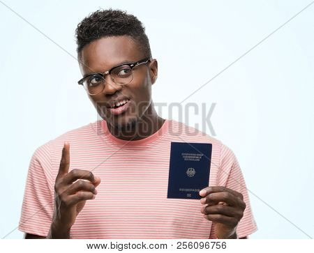 Young african american man holding a german passport surprised with an idea or question pointing finger with happy face, number one