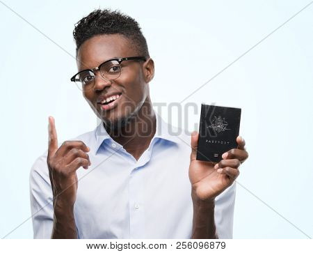 Young african american man holding australian passport surprised with an idea or question pointing finger with happy face, number one