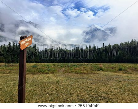 A Wood Sign Labeled Mount Robson And Pointing To Mount Robson Far Off In The Distance In Beautiful B