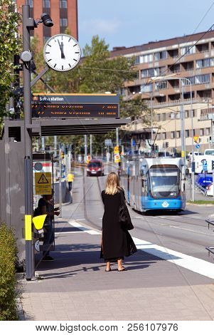 Solna, Sweden - August 24, 2018: A Woman In Black Dress Waiting For A Tram Ath The Tram Stop Solna B