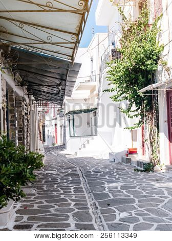 Beautiful narrow street with white houses in Mikonas island, Greece. Traditional narrow street with white facedes of buildings and blue doors