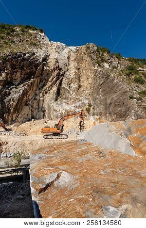 Orange Tracked Excavator With The Jackhammer In A Marble Quarry (carrara White Marble) In The Apuan 