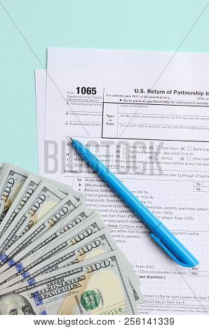 1065 Tax Form Lies Near Hundred Dollar Bills And Blue Pen On A Light Blue Background. Us Return For 