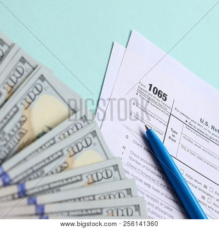 1065 Tax Form Lies Near Hundred Dollar Bills And Blue Pen On A Light Blue Background. Us Return For 