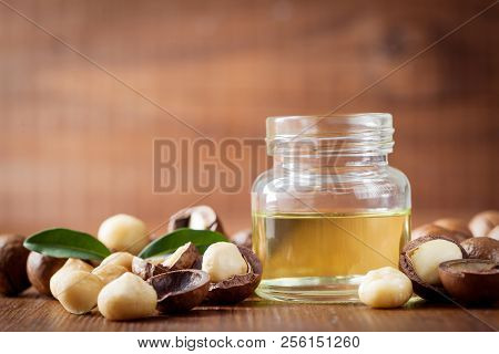 Jar With Macadamia Oil And Heap Of Nuts On Wooden Rustic Table.
