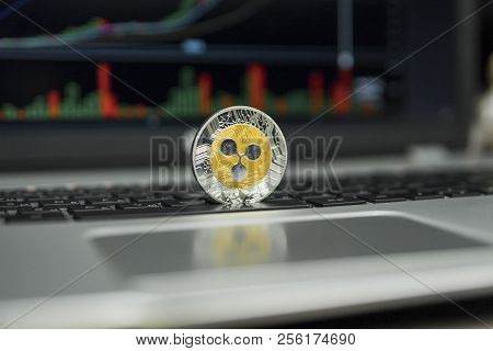 Golden And Silver Ripple Coin On A Black Keyboard Of Silver Laptop And Diagram Chart Graph On A Scre