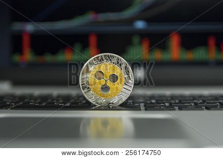 Golden And Silver Ripple Coin On A Black Keyboard Of Silver Laptop And Diagram Chart Graph On A Scre