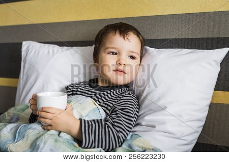 Sick Upset Cute Curing Boy Lying On Bed On Pillow Under Blanket Taking Medicament In Cup