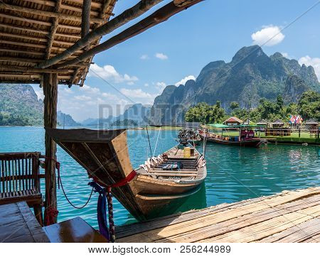 Wooden Thai Traditional Long-tail Boat And Floating Wooden Houses On A Lake With Mountains And Rain 
