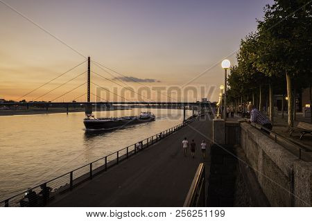 A Cargo Boat Travelling Along The River Rhine At Dusk In Dusseldorf, Germany.