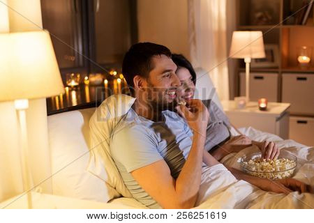 people, family and leisure concept - couple with popcorn watching tv at night at home