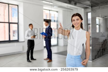 real estate business, sale and people concept - happy smiling realtor or businesswoman with folder showing thumbs up and customers at new office room