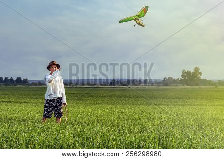 Boy On A Green Field Pointing Finger At A Flying Paraglider. Copy Space.