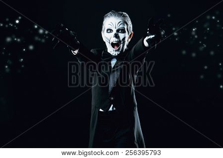 Portrait of a child boy with carnival make-up of a skeleton wearing elegant tail-coat. Studio shot over black background. Halloween. Dia de los muertos. The Day of the Dead.