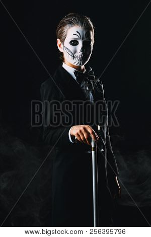 Portrait of a child boy with carnival make-up of a skeleton wearing elegant tail-coat. Studio shot over black background. Halloween. Dia de los muertos. The Day of the Dead.
