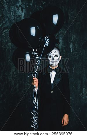 Portrait of a child boy with carnival make-up of a skeleton wearing elegant tail-coat. Studio shot over dark grunge background. Halloween. Dia de los muertos. The Day of the Dead.