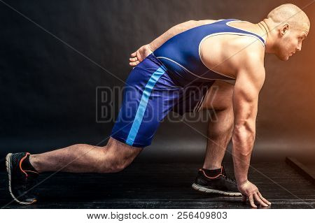A Young Athletic Man In Blue Wrestling Tricky And Blue Shorts Makes A Stretch On A Black Isolated Ba