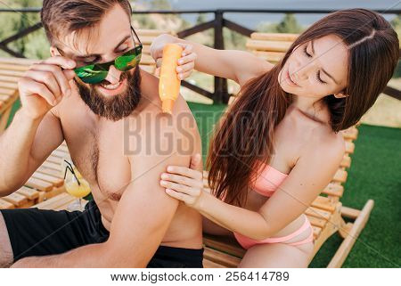 Careful Girl Sits Behind Guy And Puts Some Sunproof Cream On His Shoulders. Also Woman Rubs Them And