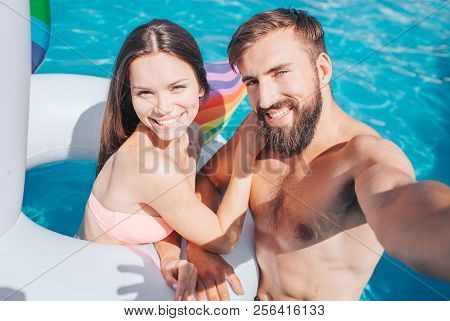 Guy And Girl Are In Swimming Pool. She Is In Air Mattress. Young Man Holds Camera. They Look At It A
