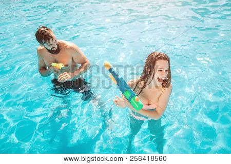 A Picture Of Guy Attacking Girl In Swimming Pool. He Is Shooting From Water Gun. Girl Is Trying To D