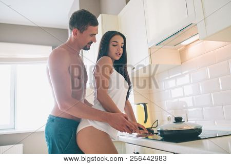 Sexual And Sensitie Picture Of Couple Standing Together In Kitchen. He Holds Hands On Hers. Girl Kee