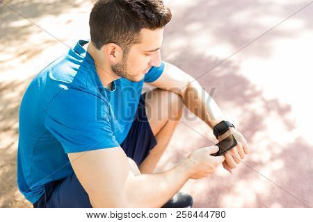Overhead Above Shot Of Jogger Syncing His Smart Watch With Smartphone While Sitting In Park