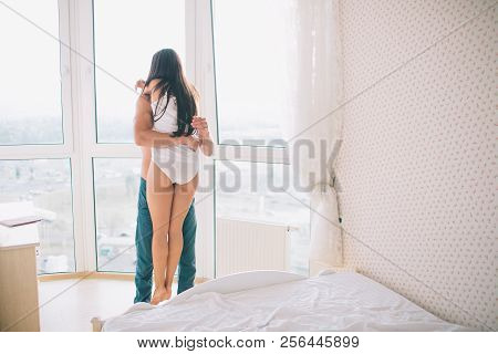 A Picture In Bedroom Where Guy Holds Girl With Hands. He Embrace Her. Girl Keeps Her Hands On His Ne