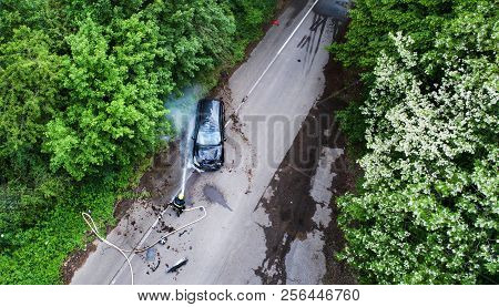 A Firefighter Extinguishing A Burning Car After An Accident. Top View.