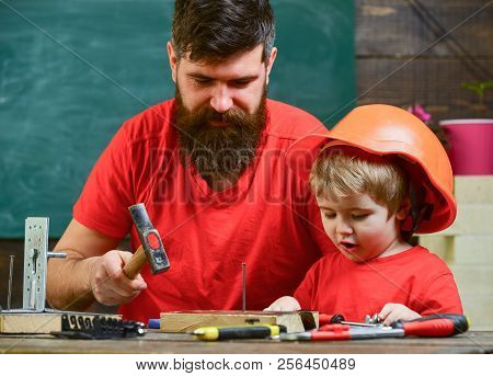 Boy, Child Busy In Protective Helmet Learning To Hammering Hobnails With Dad. Workshop And Handyman 
