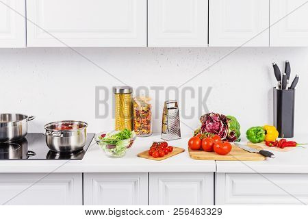 Ripe Vegetables On Cutting Boards, Pans On Electric Stove In Light Kitchen