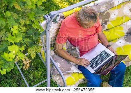 Top View Of Eldery Man Sitting And Relaxing On A Summer Holiday Rasort Using Laptop On Grass On Couc